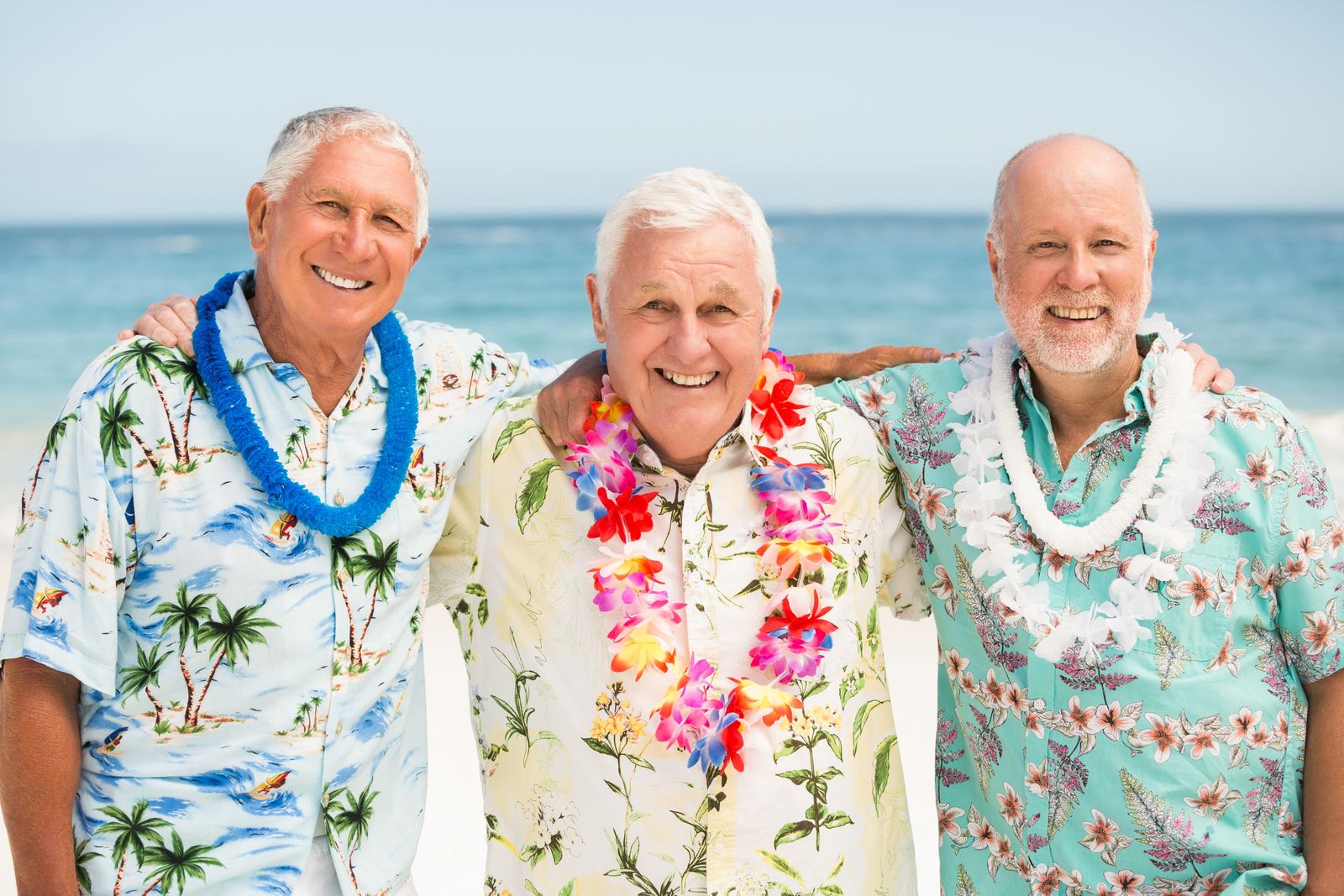 Three friends in aloha shirts and lei smiling on a Maui beach