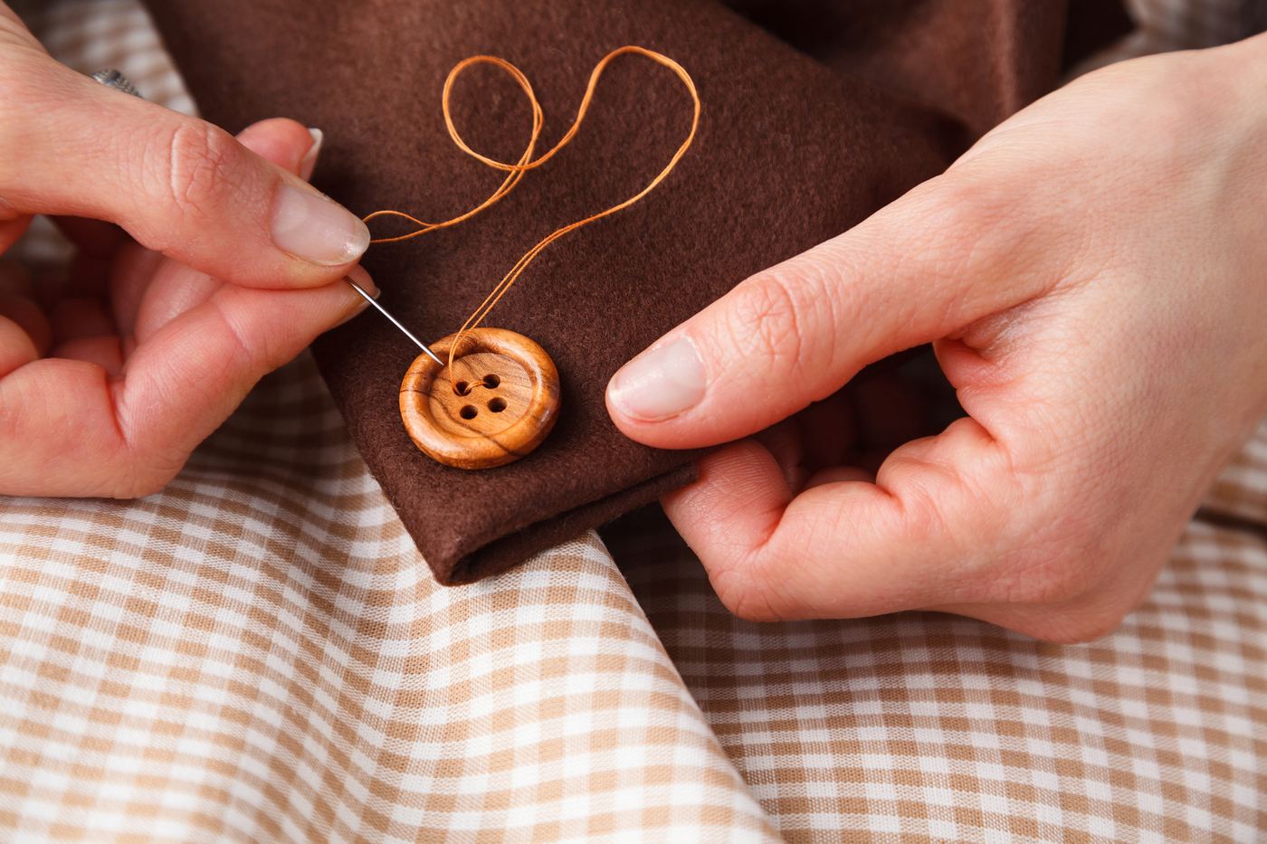 Hands sewing a wooden button onto a brown coat