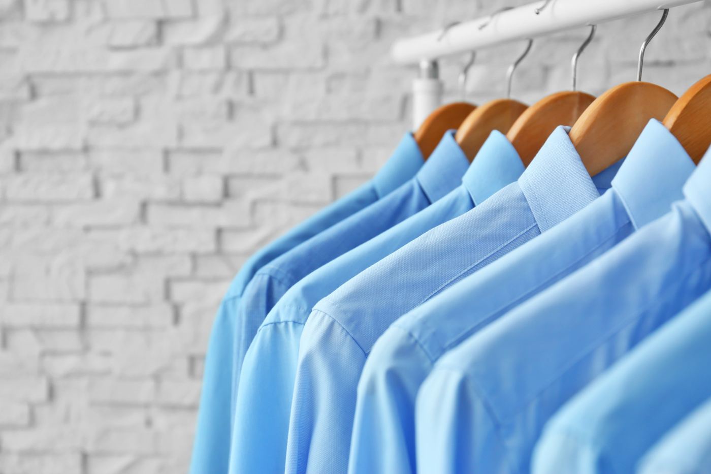 Row of pressed light-blue dress shirts on wooden hangers
